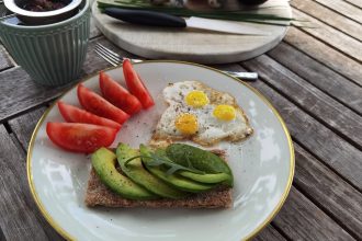 A vibrant outdoor breakfast setup with avocado toast, quail eggs, tomatoes, and tea.