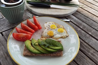 A vibrant outdoor breakfast setup with avocado toast, quail eggs, tomatoes, and tea.