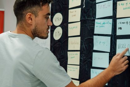 A man in a casual t-shirt organizes notes on a wall, focusing on a 'WORK OUT' sign.
